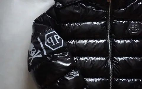 Błyszcząca, czarna kurtka Philipp Plein z futrzanym kapturem i białym logo na rękawie.