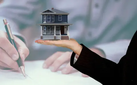Model domu na dłoni, podczas gdy ktoś podpisuje dokumenty. Kluczowe pytanie: do kiedy rozliczenie za wynajem mieszkania?