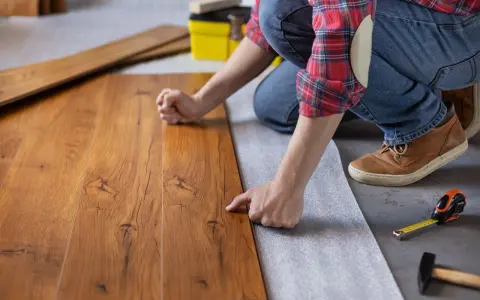 Persona posiziona assi di legno su un tappetino isolante, un passo fondamentale per come insonorizzare il pavimento e ridurre i rumori.