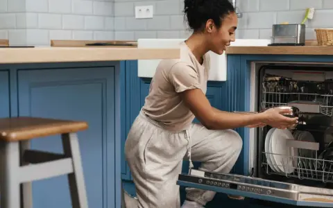 Une femme charge son lave-vaisselle encastrable. Elle place une casserole dans le panier inférieur.