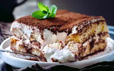 Tiramisú cremoso cubierto de cacao y decorado con menta.