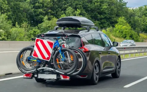 Auto in autostrada con due biciclette sul retro e box sul tetto. Il carico sporgente è ben visibile, pronto per un'avventura.