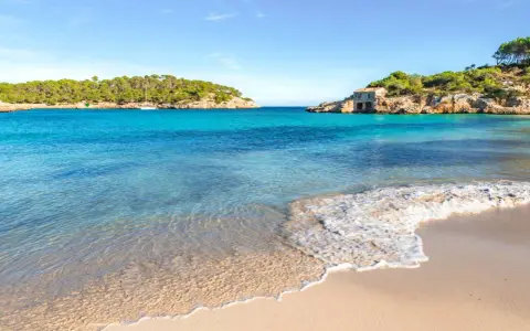 Türkisfarbenes Meer, Sandstrand und felsige Küste mit einem kleinen Haus auf Mallorca.