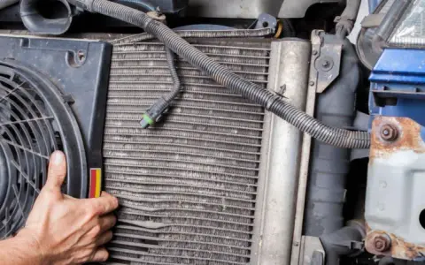 Mechanic inspects car's condenser, noting bent fins and corrosion, common symptoms of a bad condenser.