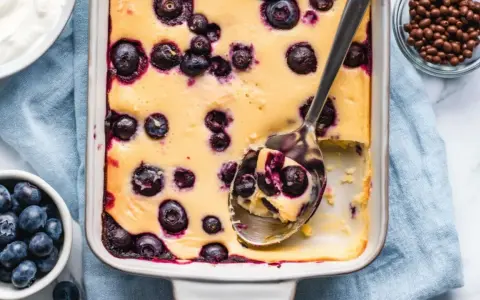 Ein cremiger Quarkauflauf low carb mit Blaubeeren, frisch aus dem Ofen. Eine Löffelportion zeigt die saftige Konsistenz.