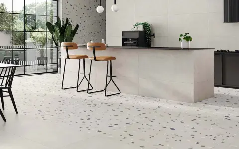 Suelos para cocinas blancas con diseño de terrazo moteado, isla central con taburetes y grandes ventanales.
