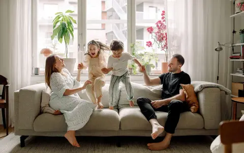 Familjen hoppar glatt på soffan i detta hemma hos reportage. Barnen skrattar högt medan föräldrarna ler.