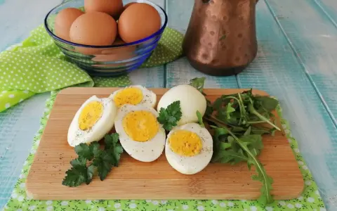 Uova sode in friggitrice ad aria, tagliate a metà, su tagliere con rucola e prezzemolo. Un modo sano e veloce per preparare le uova.