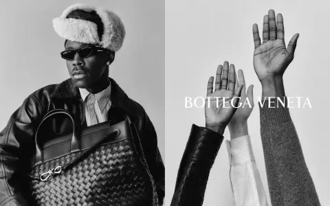 Uomo con cappello di pelliccia e borsa Bottega Veneta, mani alzate. Un omaggio alla storia del brand.
