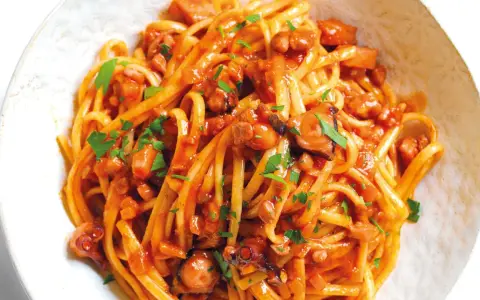 Linguine al ragù di pesce, un piatto saporito con polpo e pomodoro, guarnito con prezzemolo fresco.