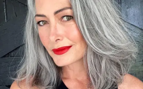 Donna con splendidi capelli grigi, labbra rosse vivaci e uno sguardo intenso.