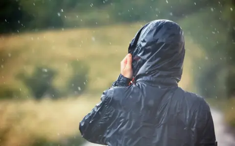 Person im Regen, die Kapuze einer Jacke mit PU-Beschichtung festhält.