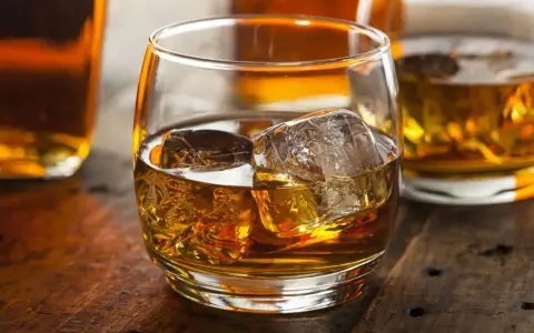 Szklanka złocistego trunku z lodem, obok butelki. Dylemat: whisky szkocka czy irlandzka?
