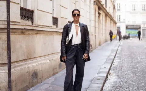 Mujer con gafas de sol y chaqueta de cuero, luciendo un elegante pantalón flare que es tendencia.