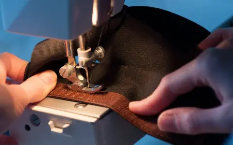 Mains habiles guidant un tissu noir sous une machine à coudre pour coudre du velcro marron.