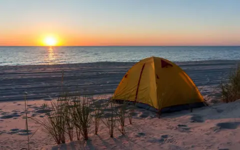 Żółty namiot na piaszczystej plaży, idealne miejsce na namioty z widokiem na zachód słońca nad morzem.