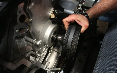 Mano retirando la polea del cigüeñal rota de un motor.
