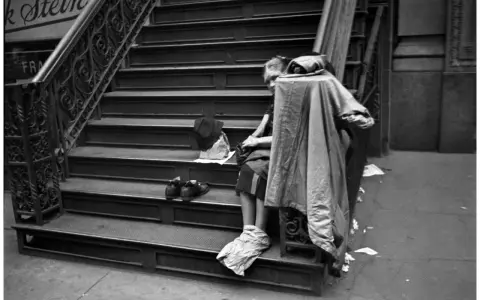 Una persona seduta sulle scale, con scarpe e cappello accanto. Un'immagine che evoca le cartier bresson foto famose, catturando un momento di vita urbana.