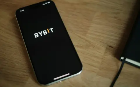 Smartfon z logo Bybit na ekranie, obok notatnik. Analiza bybit prowizje na urządzeniu mobilnym.
