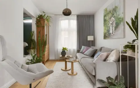 Przytulny salon w domu z szarą kanapą, wygodnym fotelem i mnóstwem zielonych roślin.