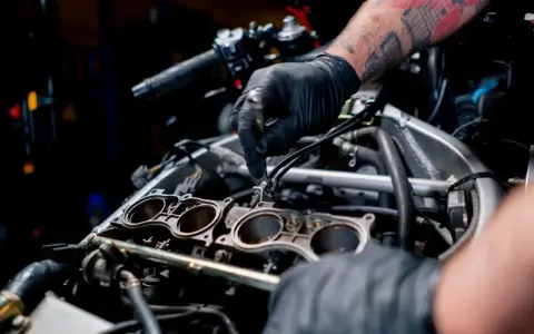 Mechanik w czarnej rękawiczce pracuje przy silniku motocykla, regulując elementy układu chłodzenia.