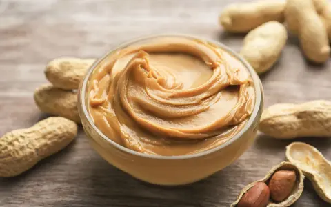 Cremige Erdnussbutter in einer Schüssel, umgeben von Erdnüssen. Ein Beweis dafür, dass erdnussbutter gesund sein kann, wenn sie in Maßen genossen wird.