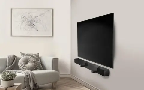 Un elegante soggiorno con un divano grigio e un quadro astratto. Al centro, un televisore a schermo piatto montato a parete con una soundbar nera.