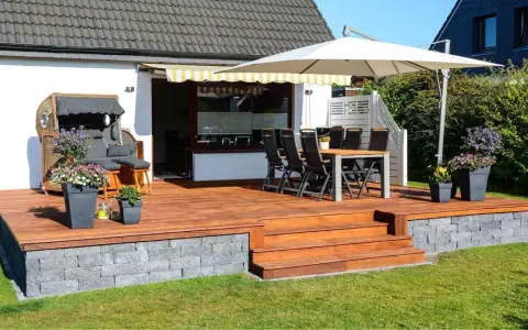 Eine 30 qm Terrasse gestalten: Holzdeck mit Sitzmöbeln, Esstisch, Sonnenschirm und Blumen. Perfekt für entspannte Stunden im Freien.