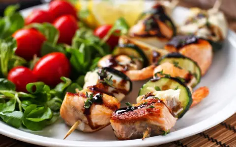 Spiedini di pesce succulenti con salmone, gamberi e zucchine, guarniti con erbe aromatiche e salsa, serviti con insalata fresca e pomodorini.