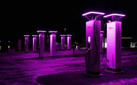 Stazione di ricarica Ionity Italia di notte, illuminata da luci viola. Colonne moderne con logo e cavi pronti per le auto elettriche.