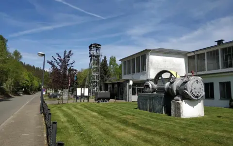 Ein historisches Bergwerk lädt zum Bergwerk besichtigen ein. Eine Förderturmanlage und alte Maschinen stehen vor dem Gebäude.
