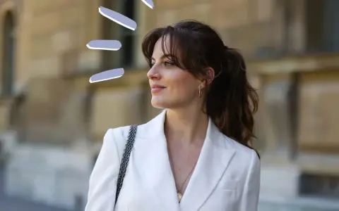 Frauen mit Curtain Bangs stylen ihre Haare lässig zu einem Pferdeschwanz. Der weiße Blazer unterstreicht den eleganten Look.