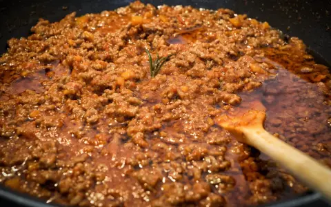 Un saporito ragù di lepre cuoce lentamente in padella, con un rametto di rosmarino che profuma l'aria.