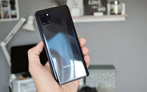 Dłoń trzyma błyszczący, czarny telefon Samsung A81 z modułem aparatów.