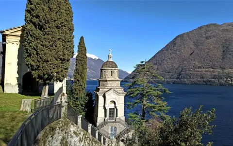 Un suggestivo lago con una piccola chiesa in mezzo, incorniciata da cipressi e montagne innevate.