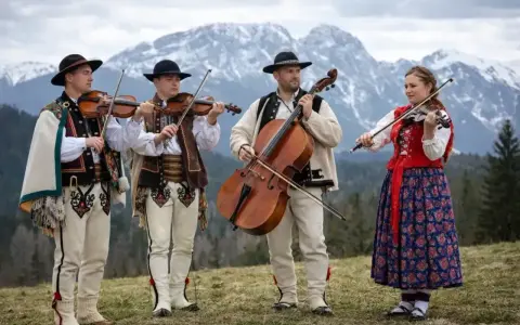 Zespół góralski z Podhala grający na skrzypcach i wiolonczeli na tle gór.