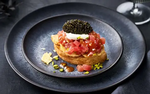Kaviar Rezepte Vorspeise: Thunfisch-Tatar auf geröstetem Brot, gekrönt mit Kaviar und einem Klecks Crème fraîche. Pistazien und Chips garnieren den Teller.