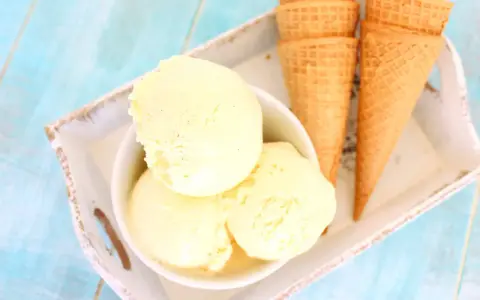 Tres bolas de cremoso helado de vainilla en un cuenco blanco, junto a conos de galleta sobre una bandeja.