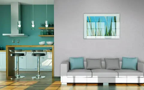 Modernes Wohnzimmer mit Vliestapete tapezieren. Ein weißes Sofa mit blauen und grauen Kissen steht vor einer Wand mit einem Bild von Gräsern. Daneben eine Küche mit Bar.