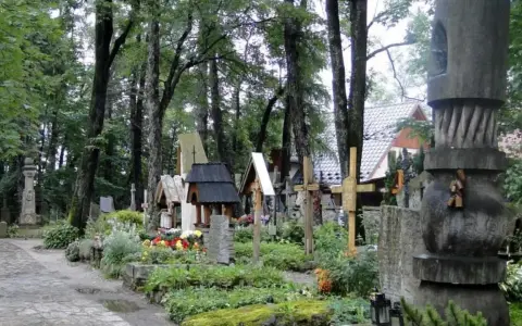 Cmentarz w Zakopanem, pełen drewnianych krzyży i rzeźb, otoczony zielenią.