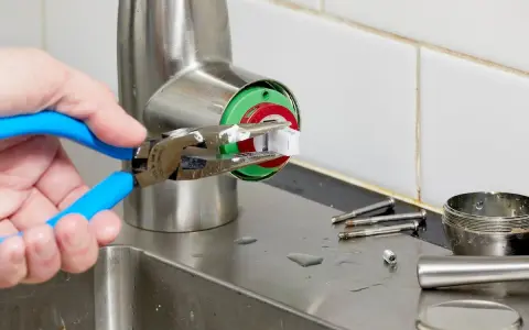 A hand uses pliers to remove a faucet cartridge, a key step in learning how to replace faucet cartridge.
