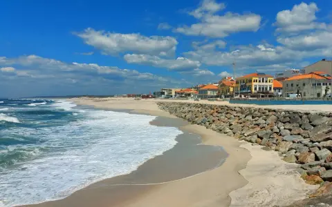 Sonne, Sand und Wellen an der Costa Verde, Portugal. Häuser mit roten Dächern säumen den Strand, geschützt von einer Steinmauer.