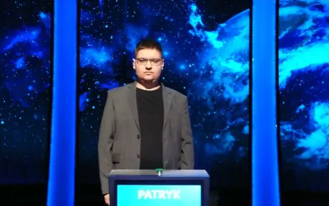 Patryk w szarym garniturze stoi przed niebieskim tłem z gwiazdami.