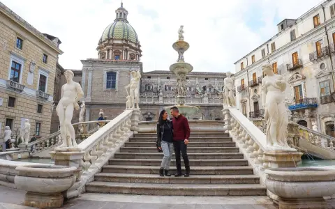 Coppia felice davanti alla Fontana Pretoria, un luogo imperdibile da vedere a Palermo, con le sue statue e la cupola in lontananza.