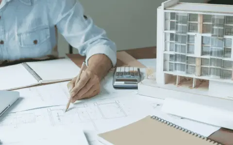 Una arquitecta de interiores dibuja planos junto a una maqueta de edificio.