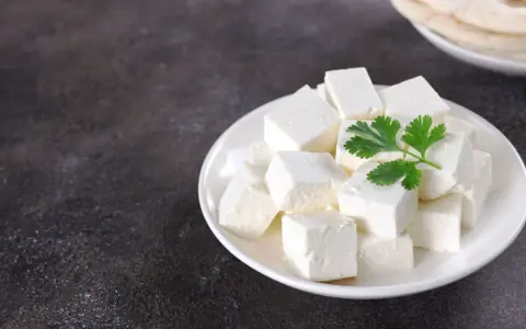 Queso paneer cortado en cubos en un plato blanco con una ramita de cilantro.