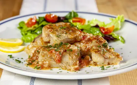 Deliziosa coda di rospo in umido con pomodoro e prezzemolo, servita con insalata fresca e spicchi di limone.