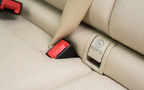 Zapięcie pasa bezpieczeństwa i oznaczenie ISOFIX na jasnej, skórzanej kanapie samochodowej. Czy baza isofix pasuje do każdego fotelika?