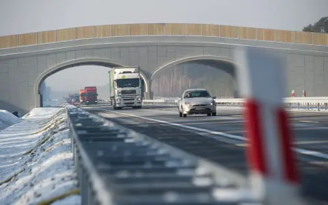 Autostrada A2 z mostem nad jezdnią, jadące samochody i ciężarówki w zimowej scenerii.