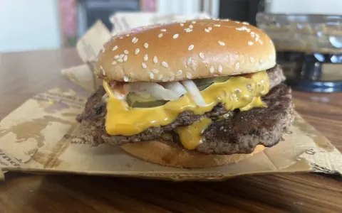 Podwójny cheeseburger z roztopionym serem, piklami i cebulą na bułce z sezamem.